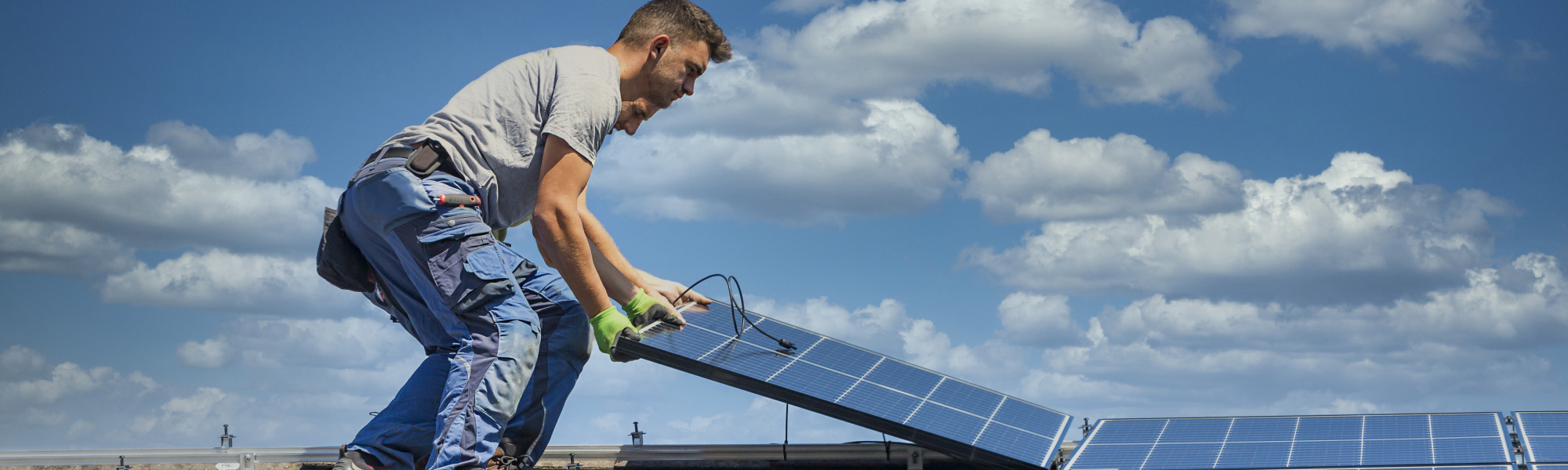 Two men lay solar panels on a roof