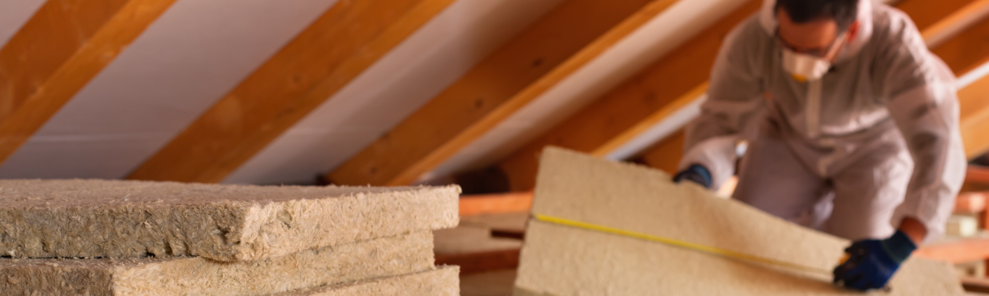 A man installs insulation between rafters