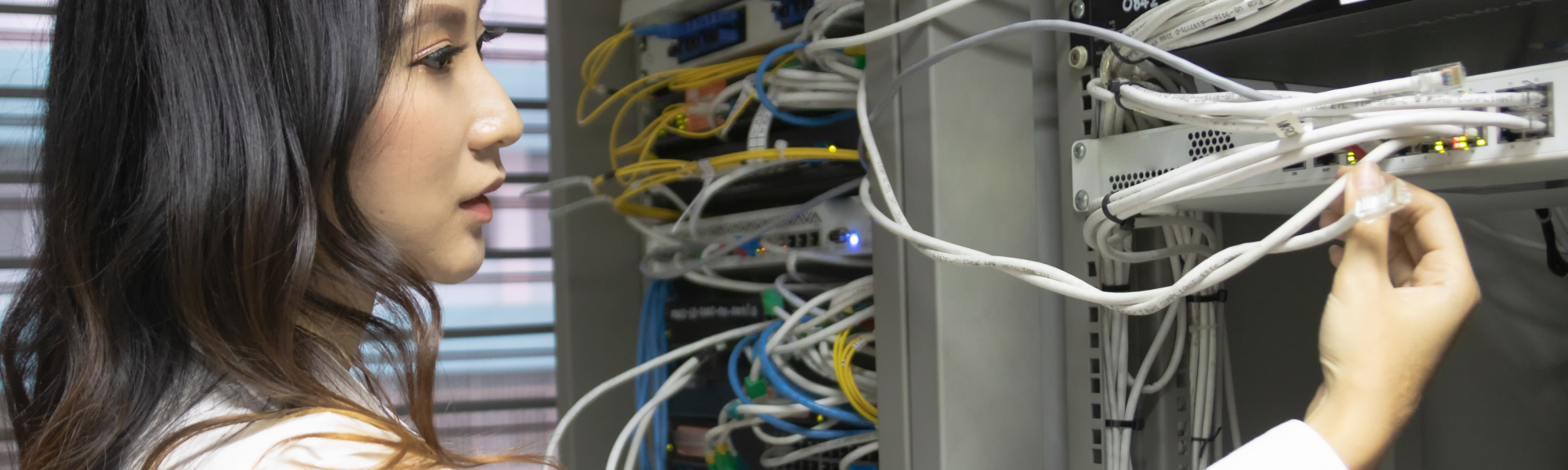 A young woman examines a connection to a switch on a server rack - advanced enterprise cybersecurity program to learn about networking