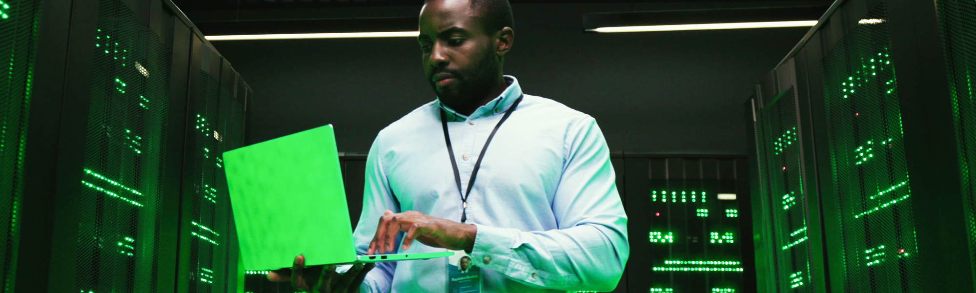 A man works on a laptop in a server room for the Advanced Cybersecurity Analyst educational program