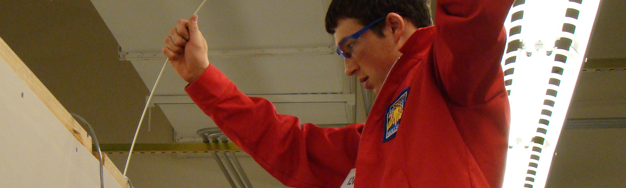 A student uses fish tape to pull AV cable through a practice wall.