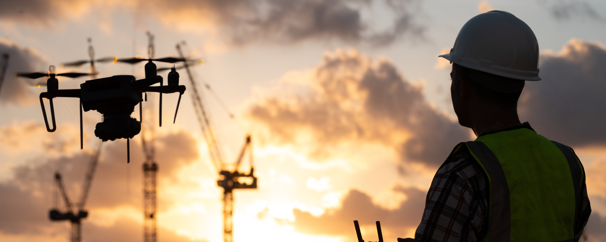 Silhouette of a construction worker flying a drone at sunset