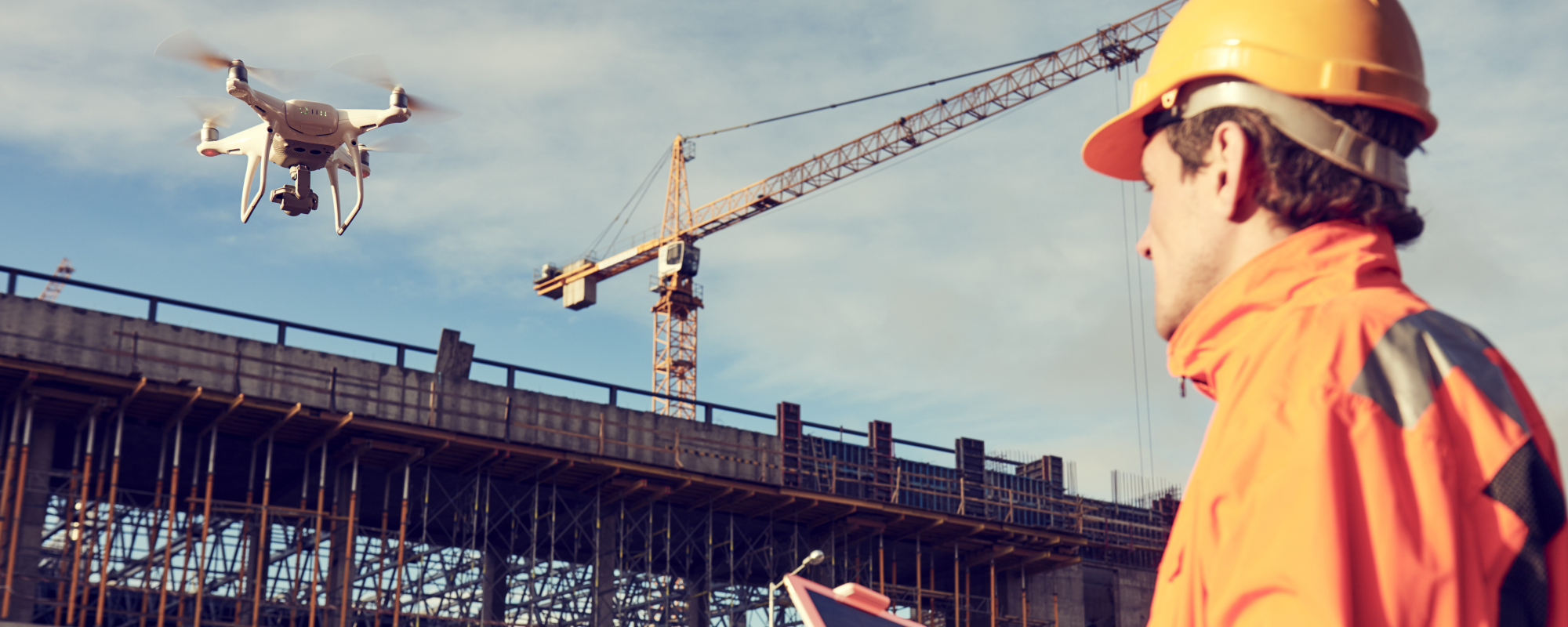 An image of a drone pilot flying a drone towards an unfinished building with a crane on top.